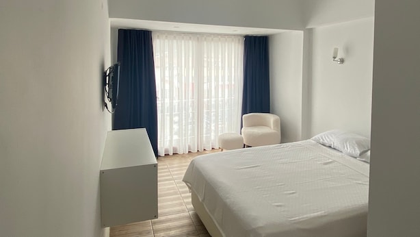 Ein modernes Hotelzimmer mit einem Bett, einem Sessel, einem Schreibtisch und einem großen Fenster mit Vorhängen.
