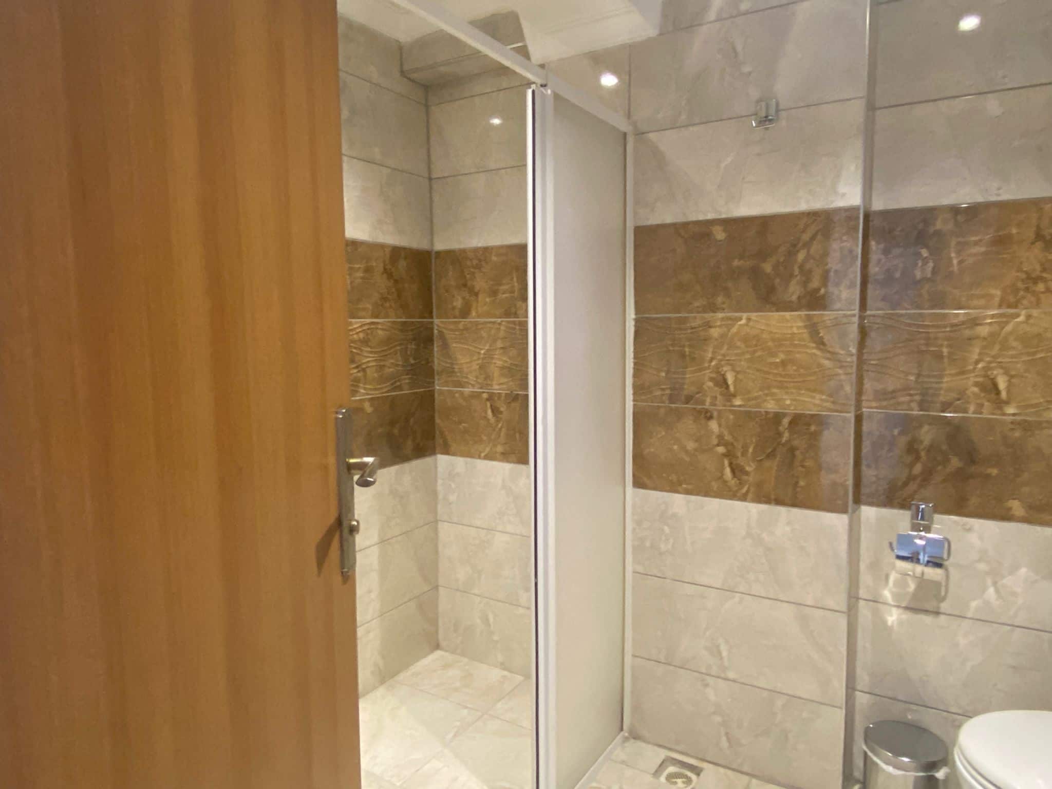 A modern bathroom with a glass-enclosed shower, a toilet, and a small trash bin.