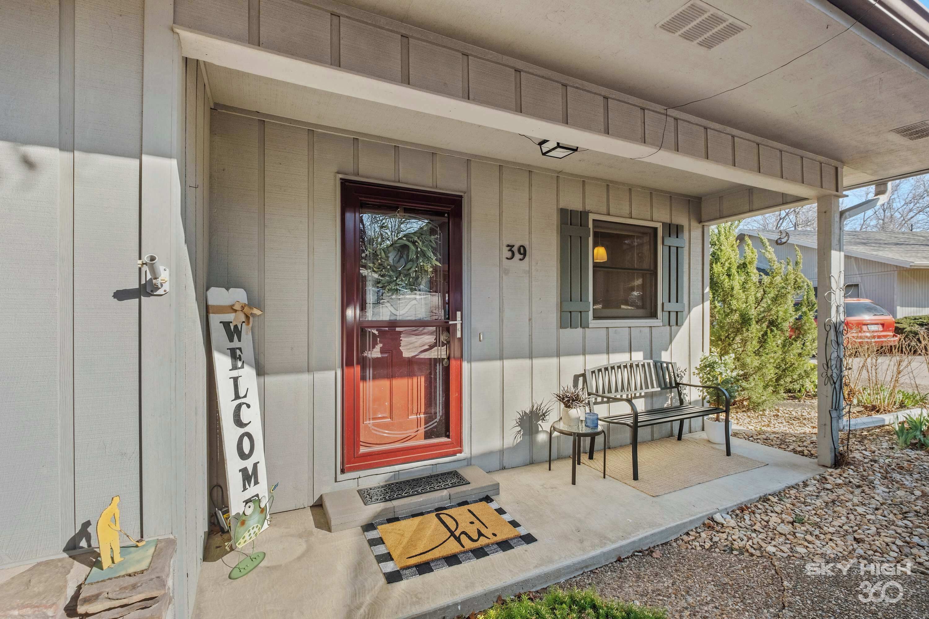 A house with a red door, a welcome sign, and a bench outside.
