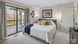 A bedroom with a large bed, a sliding glass door to a deck, a framed horse picture, and a wall-mounted light fixture. - Treetop Trailhaven-Direct Access to MTB Trails! (Bella Vista)