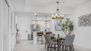 A modern kitchen with a central island, pendant lighting, and a dining area with a round table and chairs. - RIVER FLY IN: Garden View (Merritt Island)