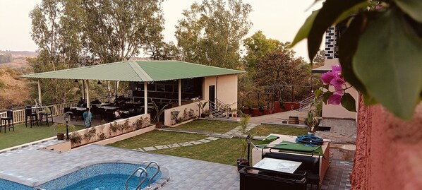 A pool area with a covered seating area, outdoor furniture, and potted plants. - Mountain Meadows Resort (Mahabaleshwar)