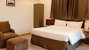 A hotel room with a bed, a brown armchair, and a matching ottoman. - Mountain Meadows Resort (Mahabaleshwar)