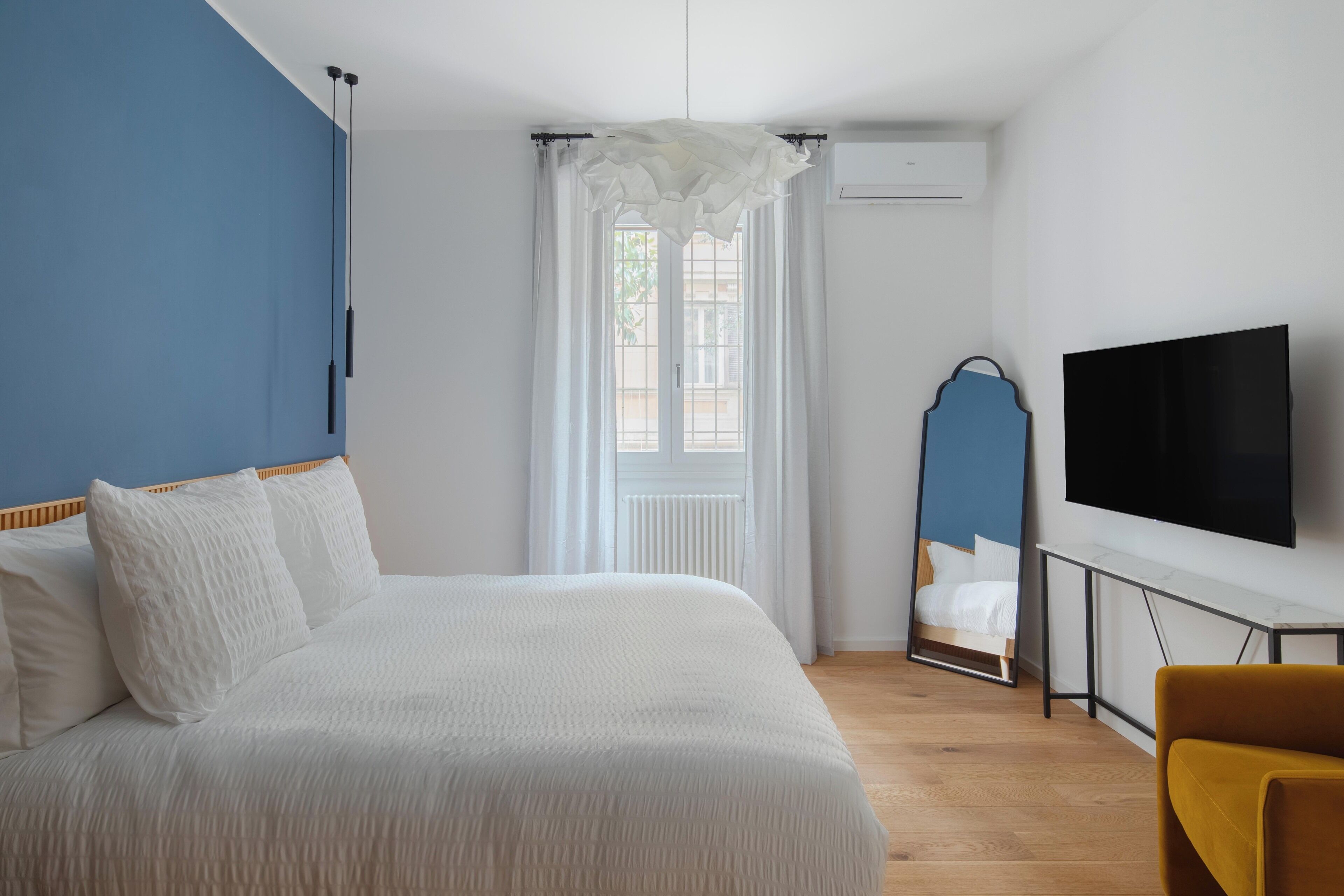 Ein Schlafzimmer mit einem Bett, einem Fernseher, einem Sessel und einem Fenster mit Vorhängen.