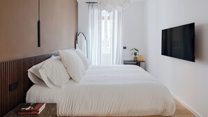 A modern bedroom with a wooden bed, a marble bedside table, a mounted TV, and a pendant light. - Cereate Suites (Rome)