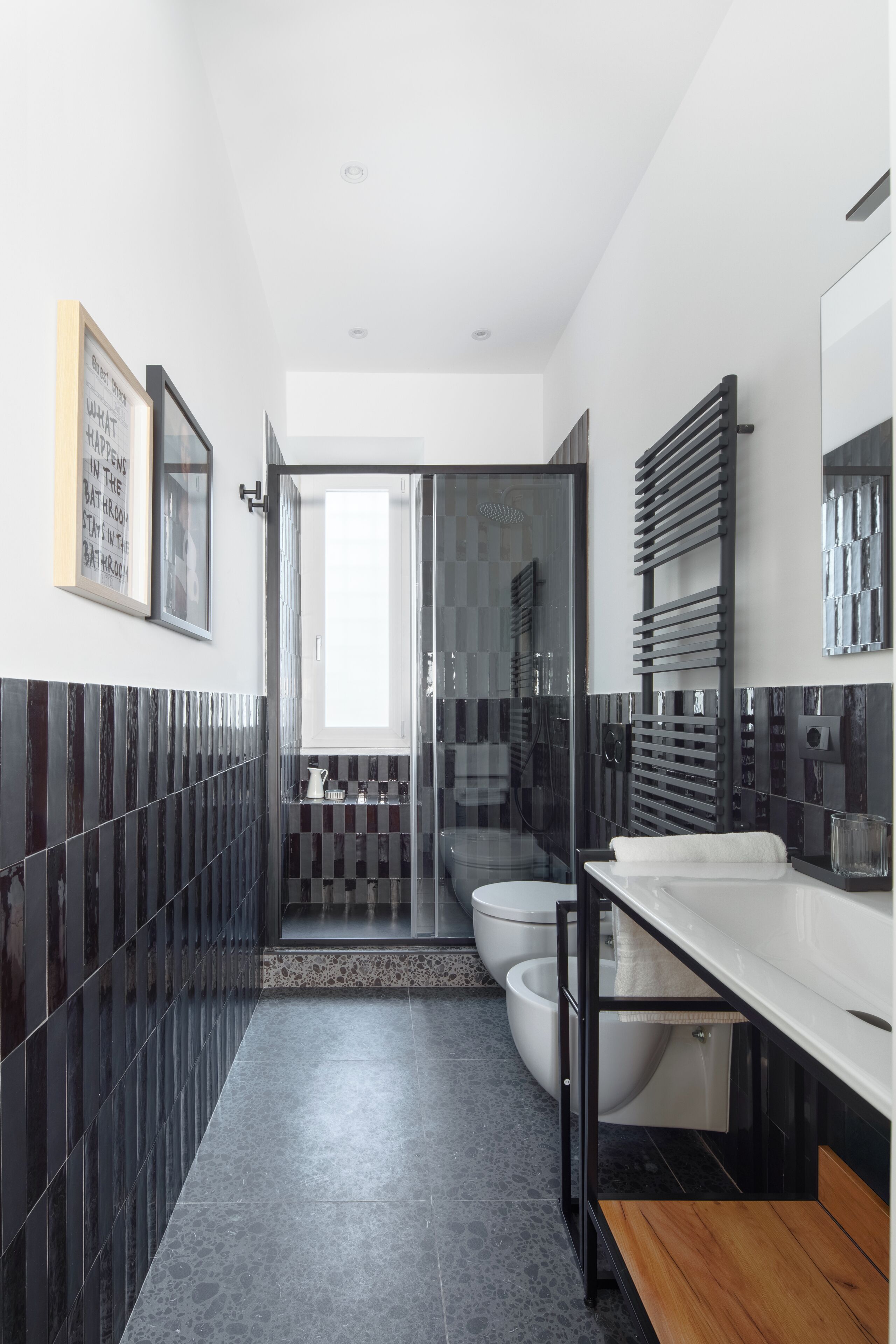 A modern bathroom with a black and white tiled backsplash, a wooden bench, and a large mirror above the sink.