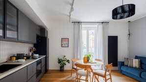A modern kitchen with grey cabinets, a black refrigerator, and a wooden dining table with chairs. There is a potted plant and a framed picture on the wall. - Cereate Suites (Rome)