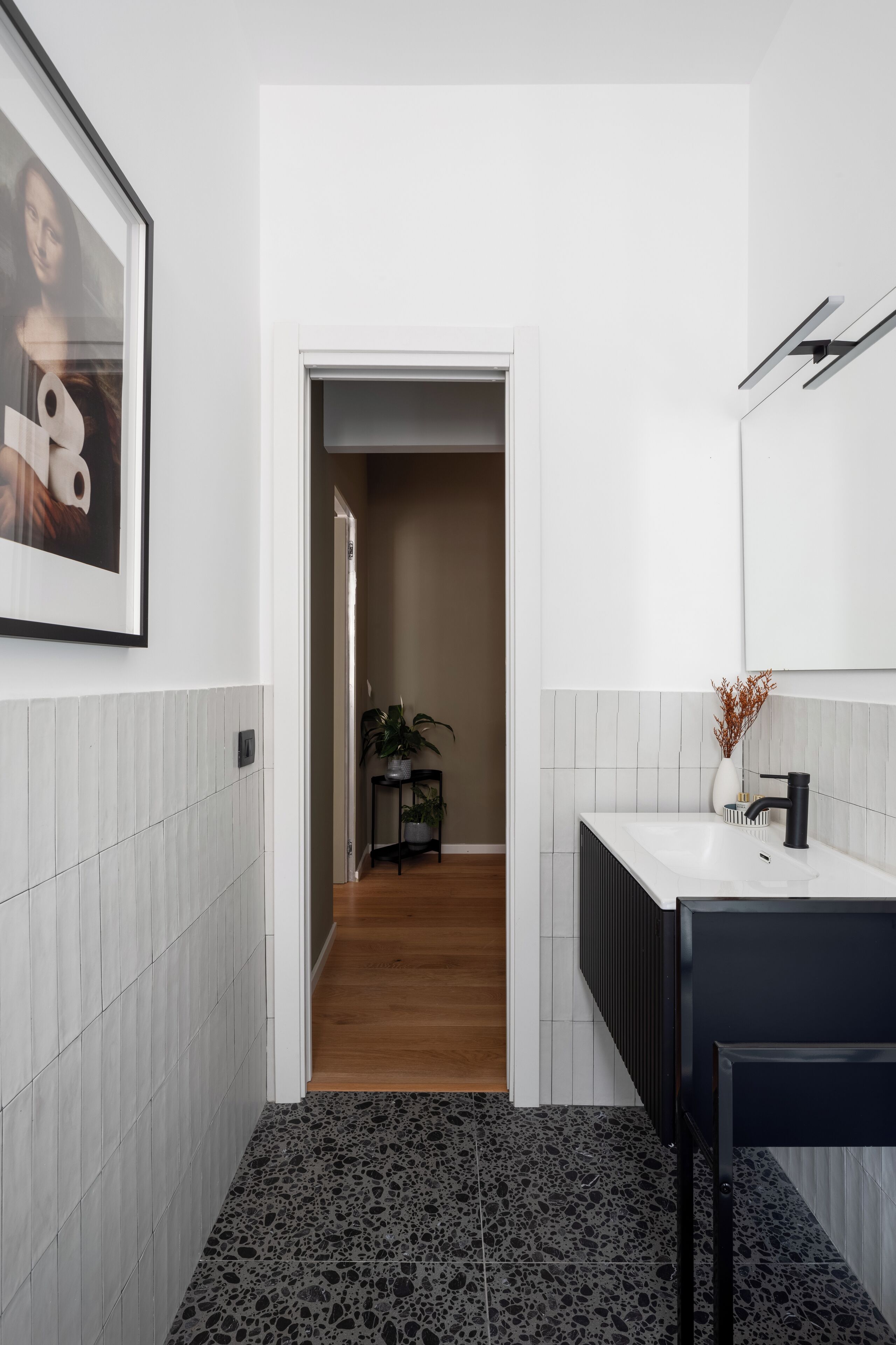 A modern bathroom with a white tiled wall, a black sink, and a framed artwork above the mirror.