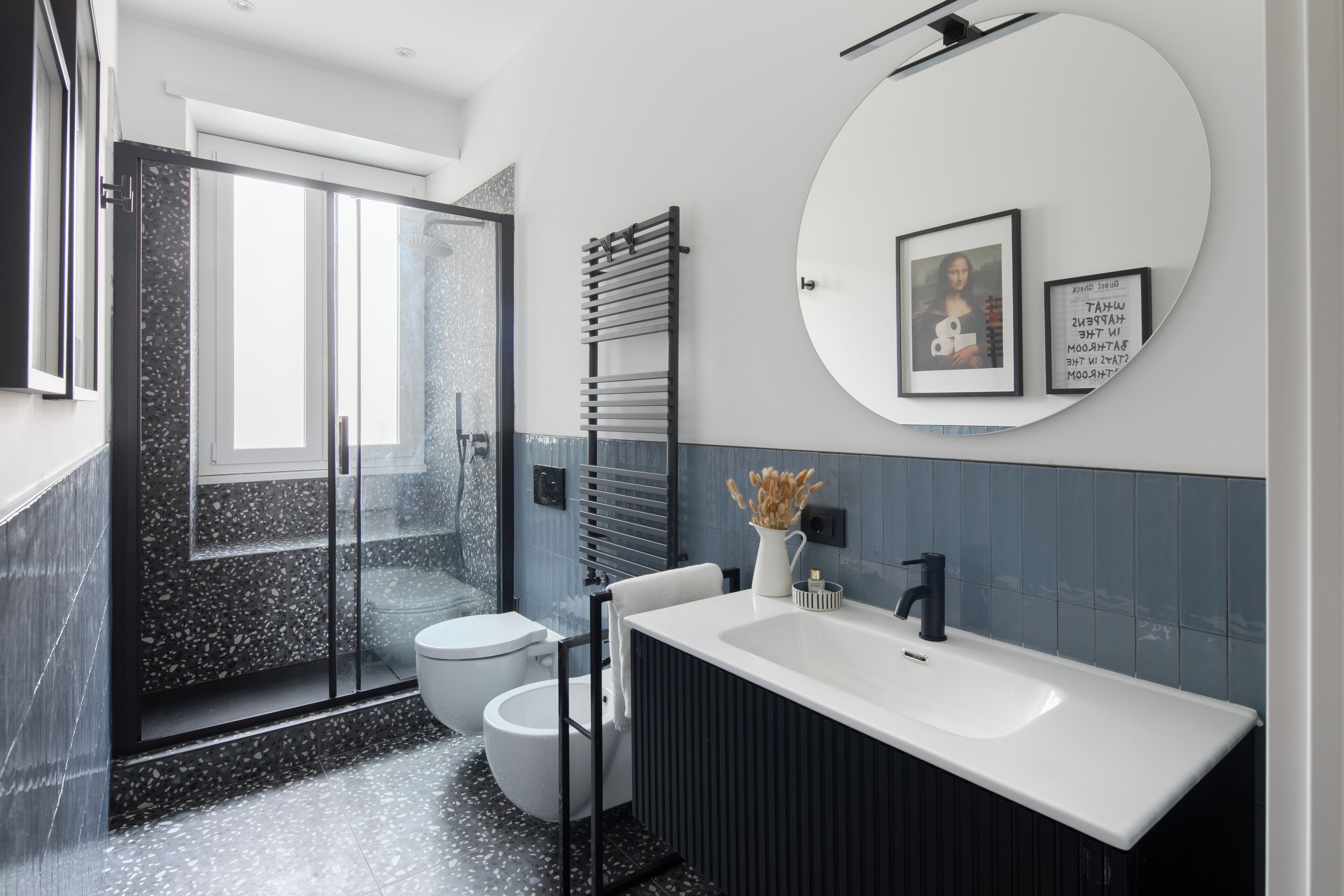 A modern bathroom with a glass shower enclosure, a white sink, and a black towel rack.