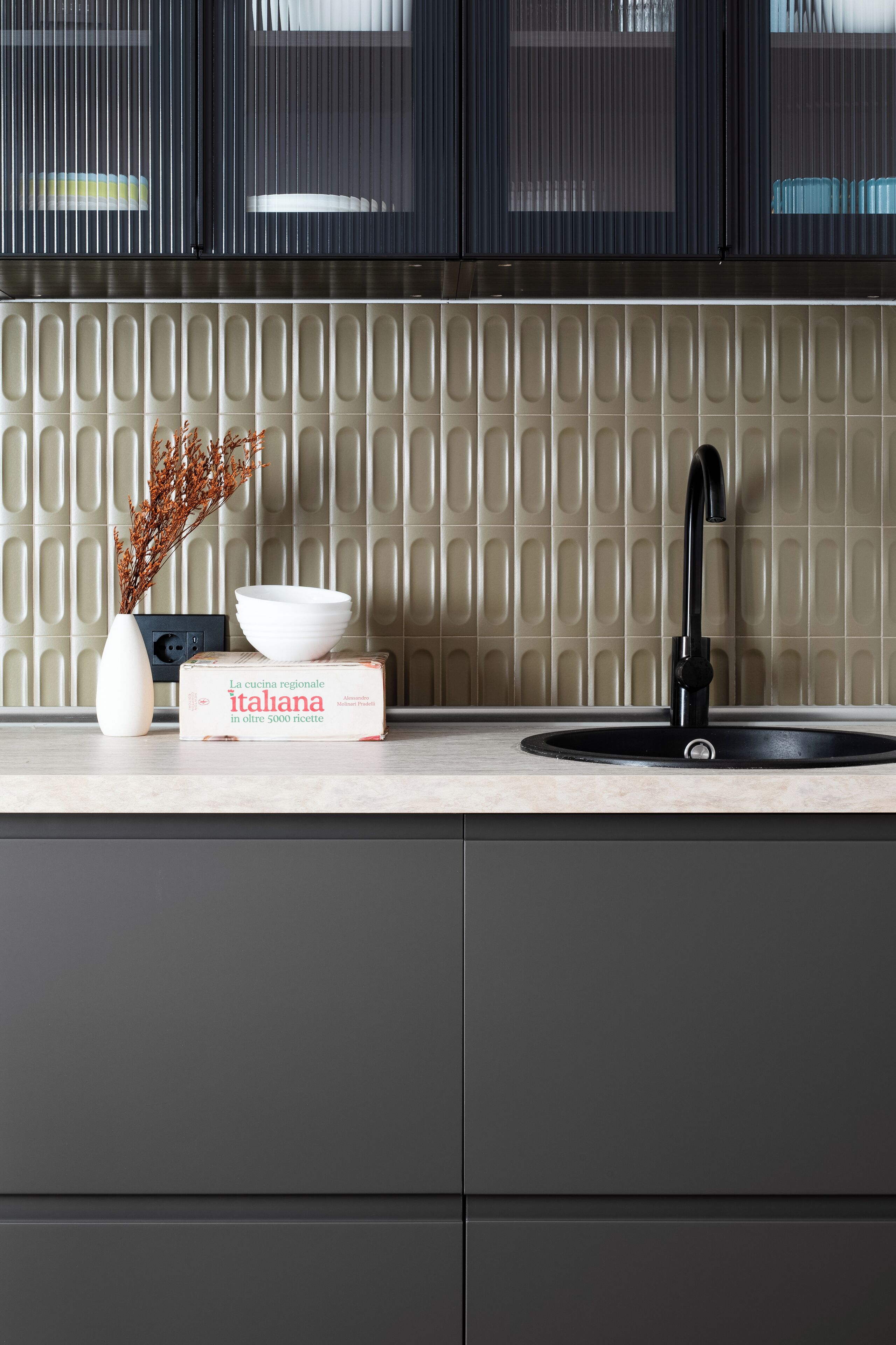 A kitchen with a modern sink, a vase with dried branches, and a box labeled "La cucina regionale italiana in oltre 5000 ricette".