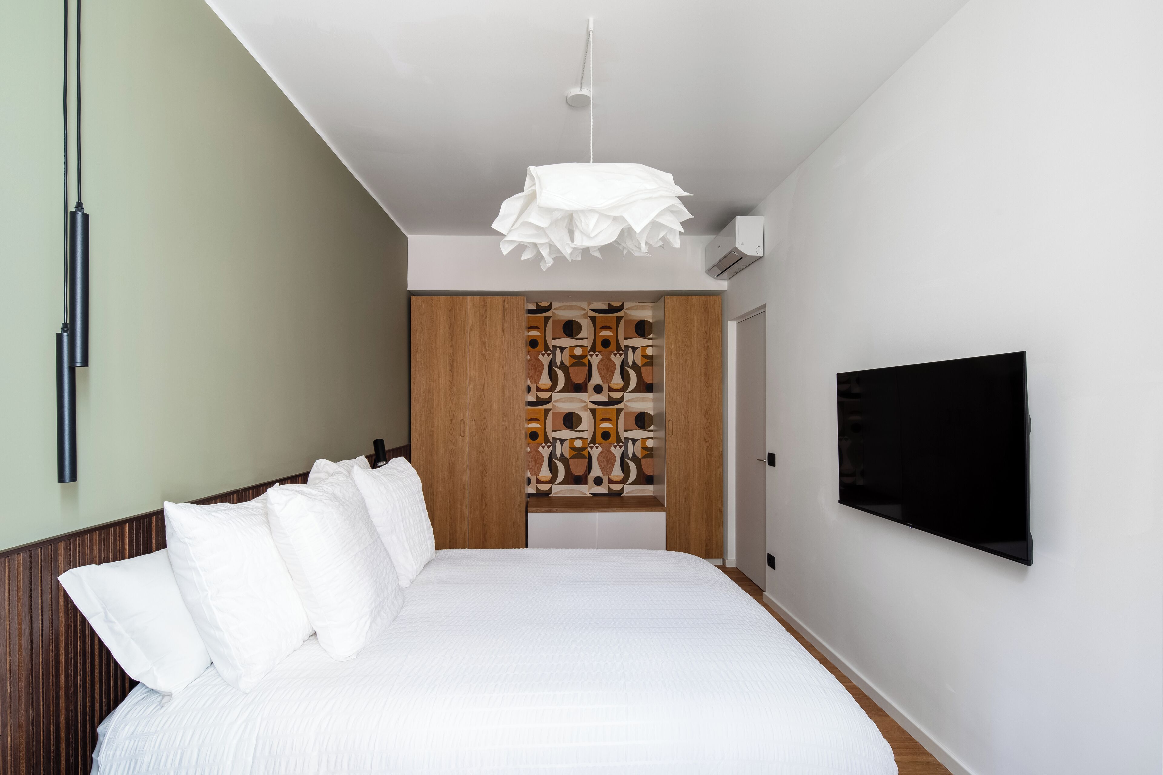 Una camera da letto con un letto grande, una TV fissata al muro e un mobiletti in legno unico con pannello posteriore decorato.