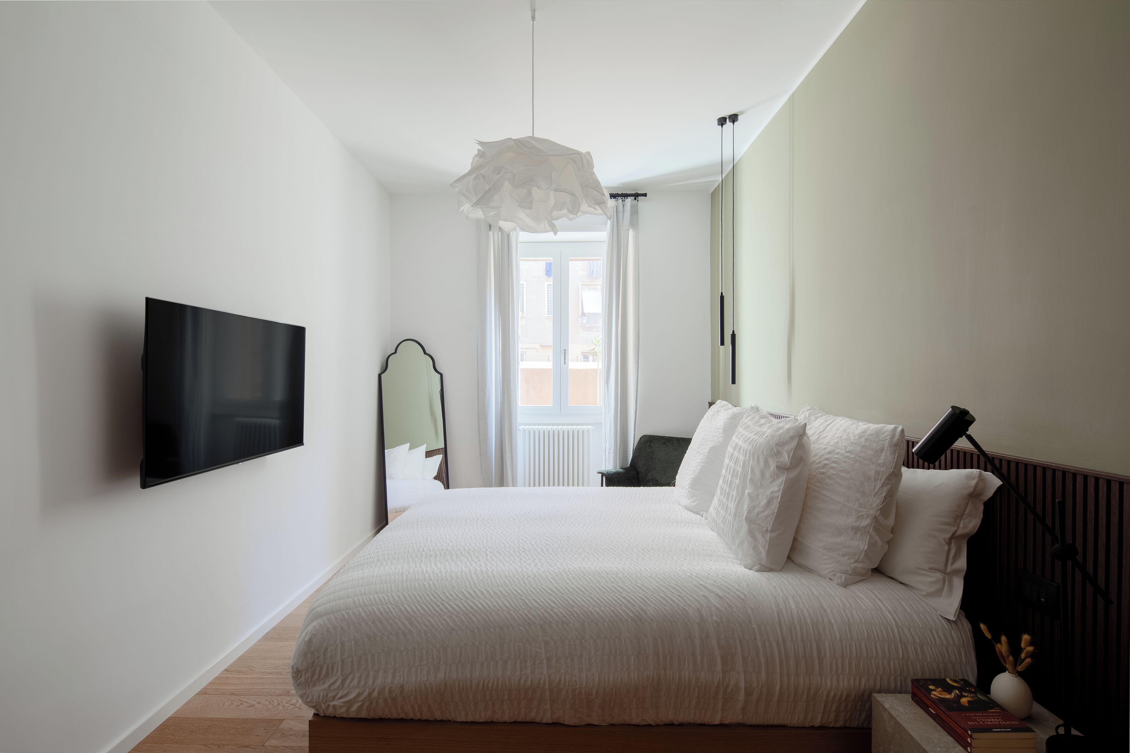 A bedroom with a bed, a flat-screen TV, a bedside lamp, and a window with curtains.