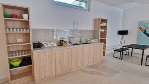 Eine moderne Küche mit Holzschränken, einer Marmor-Spritzschutzwand und einer eingebauten Spüle. Regale mit Glaskolben sowie eine kleine Essecke mit Tisch und Stühlen.