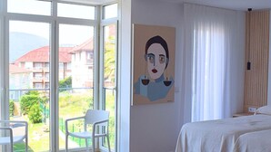 Ein Hotelzimmer mit großem Fenster, einem Bett, einem Sessel und einem Gemälde an der Wand.
