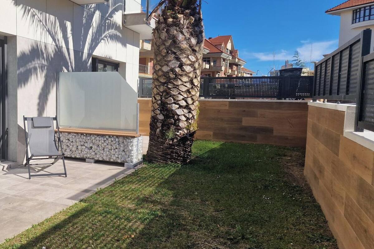 Un espacio exterior moderno con un conjunto de asientos, una jardinera de piedra y una palmera.