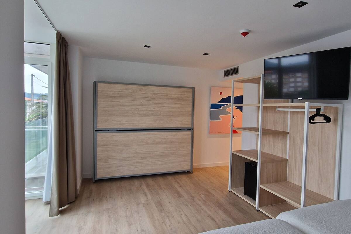 Una habitación de hotel moderna con un armario grande, un televisor montado en la pared y un balcón con cortinas.