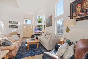 Un salon spacieux comprenant un canapé, des fauteuils, une table basse et un téléviseur. Un escalier mène à l’étage supérieur.