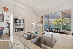 Een moderne keuken met roestvrijstalen apparatuur, een dubbele spoelbak en een eethoek met uitzicht op de omgeving.