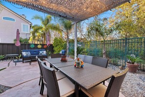 Une terrasse extérieure avec une table et des chaises, un parasol décoratif et un jardin clos.