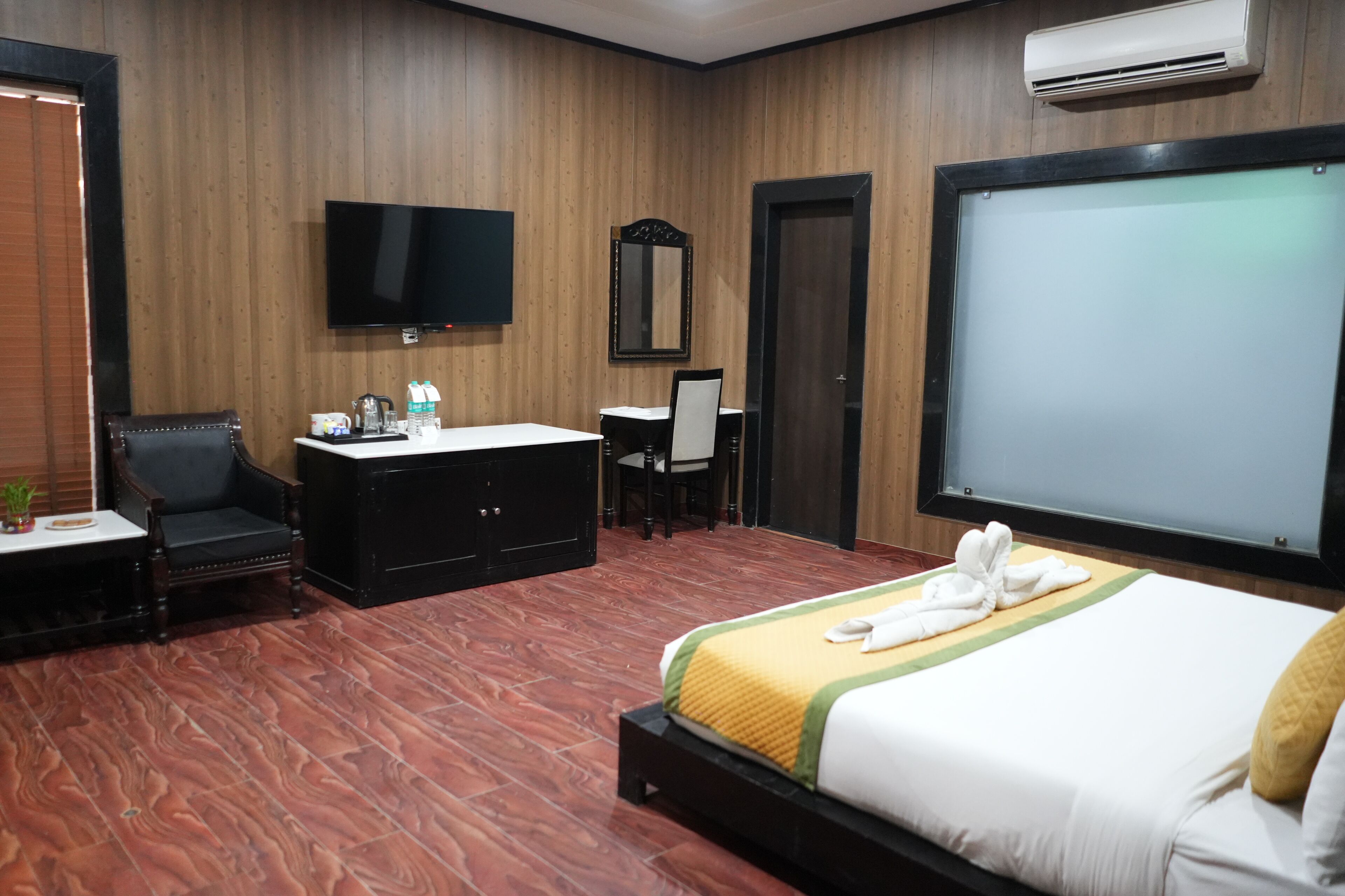 A hotel room with a large bed, a flat-screen TV, a desk with a chair, a mirror, and a wardrobe.