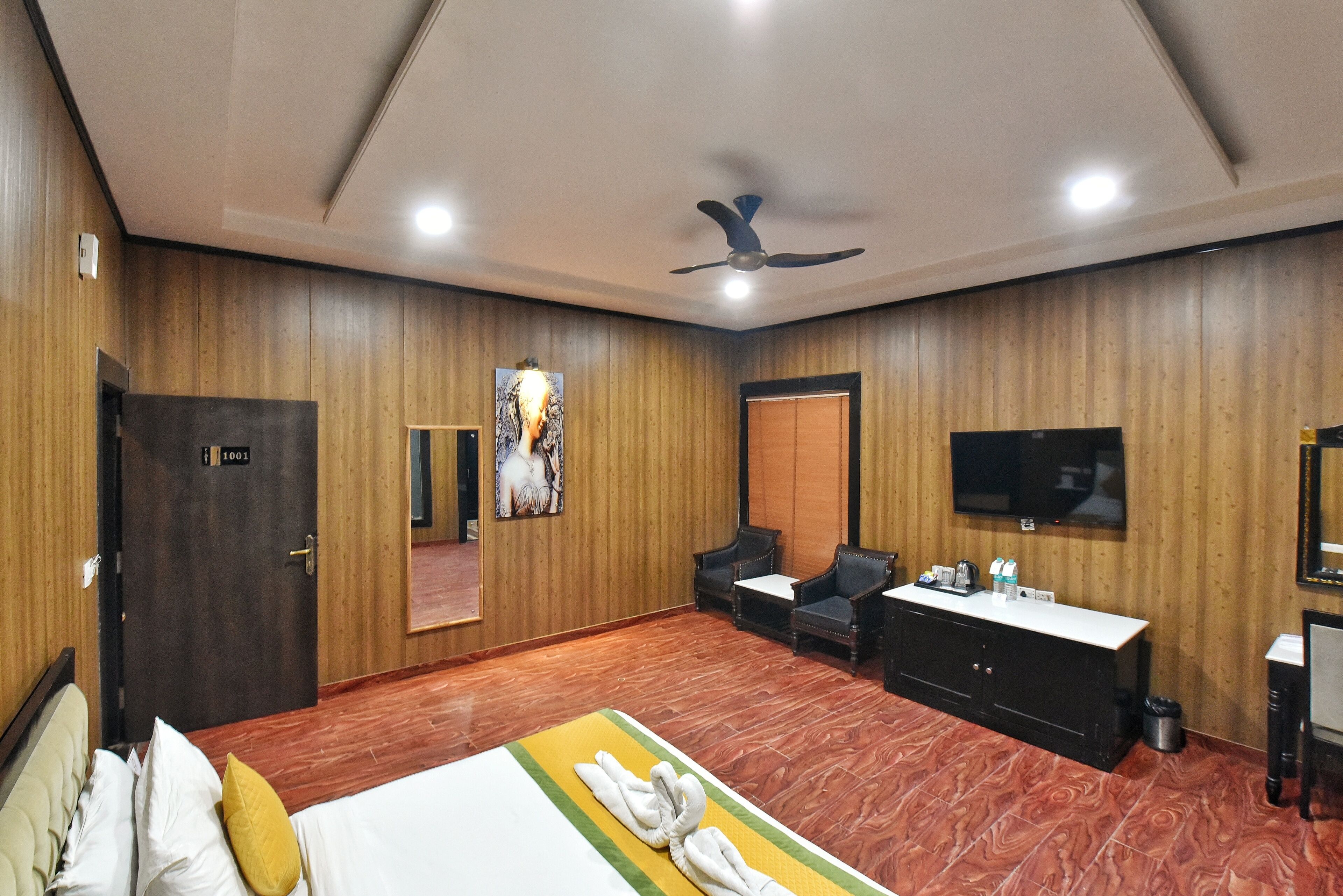 A hotel room with a bed, a desk, a chair, a television, and a ceiling fan.