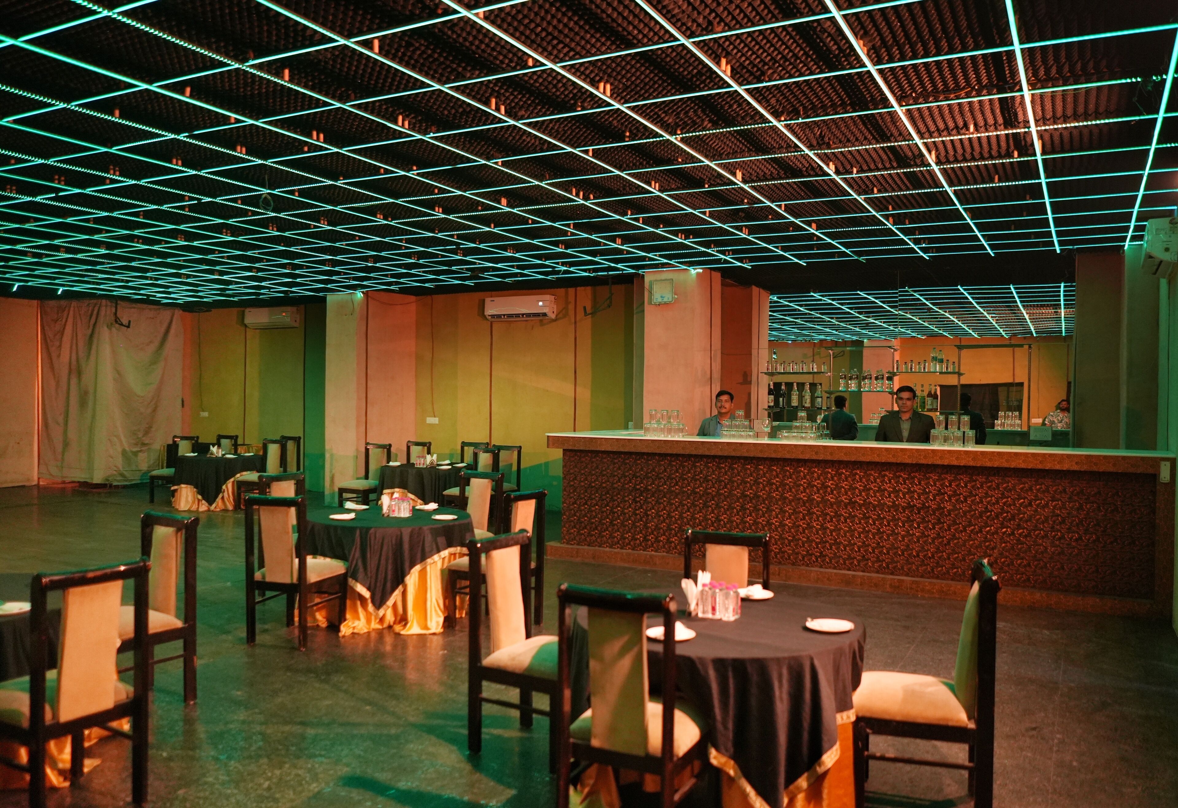 A restaurant with a grid-patterned ceiling, tables set with tablecloths and chairs, and a bar area with a counter and bar stools.