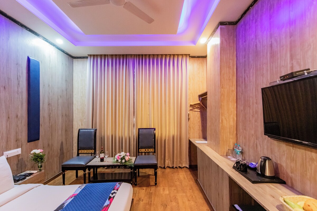 Una habitación de hotel con cama, escritorio y silla, televisión y ventana con cortinas.