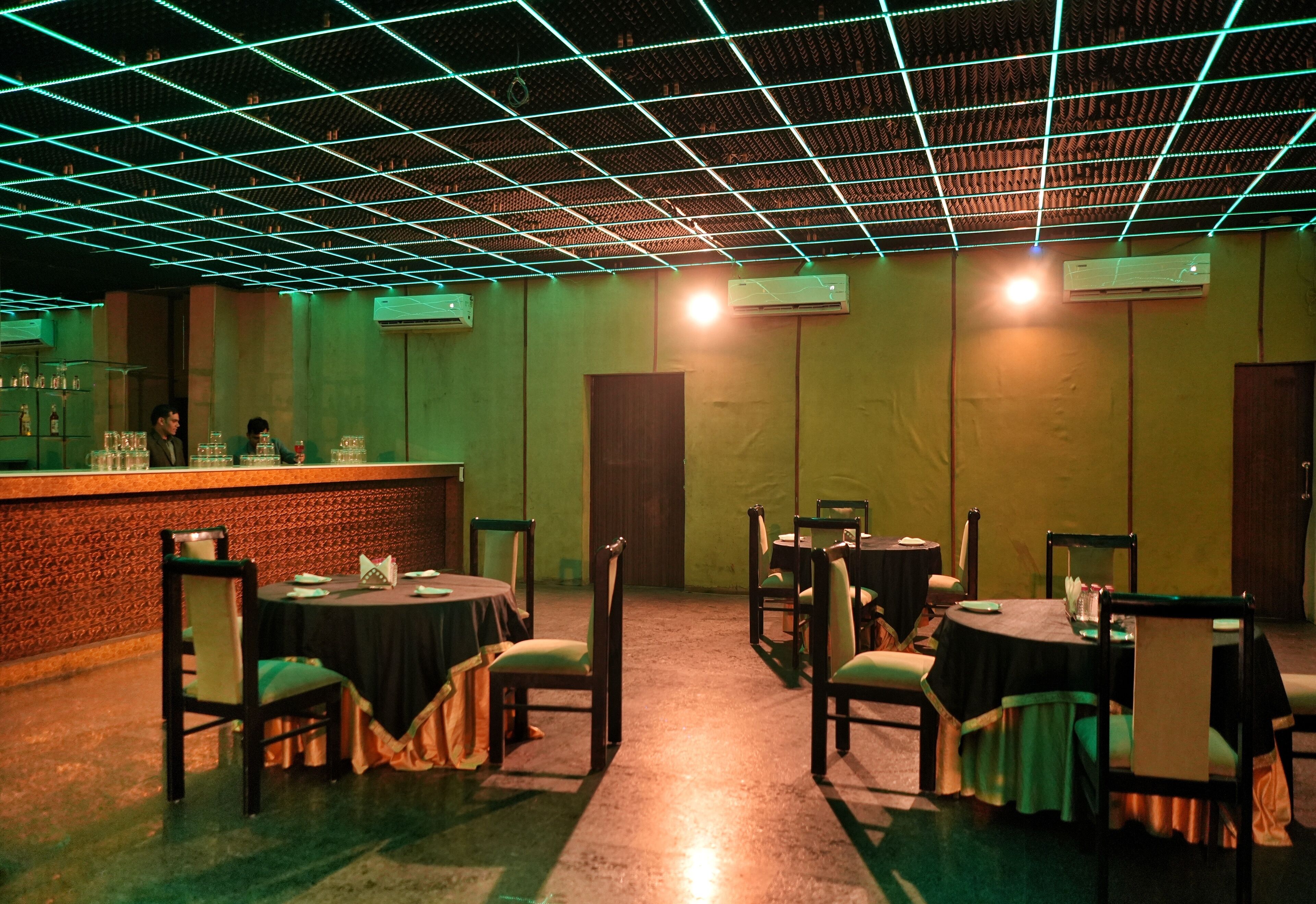 A restaurant with tables and chairs, a bar area, and a grid-patterned ceiling.
