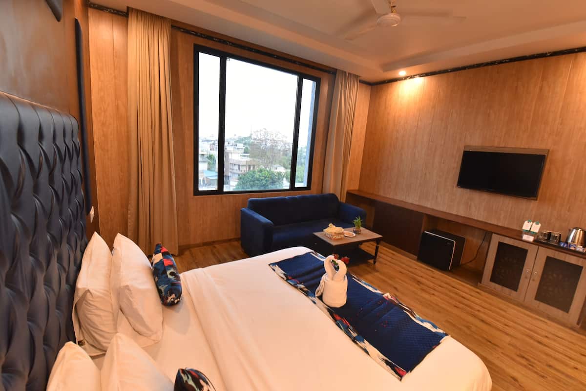 A hotel room with a large bed, a blue sofa, a flat-screen TV, and a window with a city view.