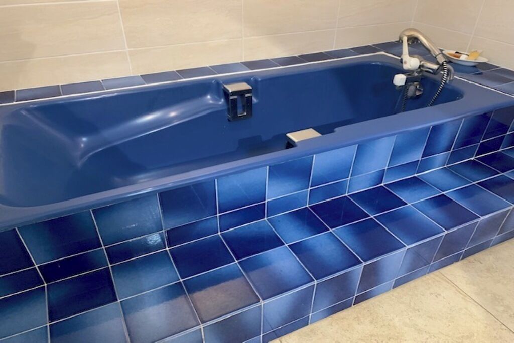 Eine blaue Badewanne mit modernem Wasserhahn und Handbrause, vor einer gefliesten Wand.