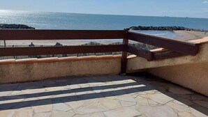 A stone patio with a wooden railing overlooking a beach. - VILLA POSEÏDON FRONTIGNAN PLAGE (Frontignan)