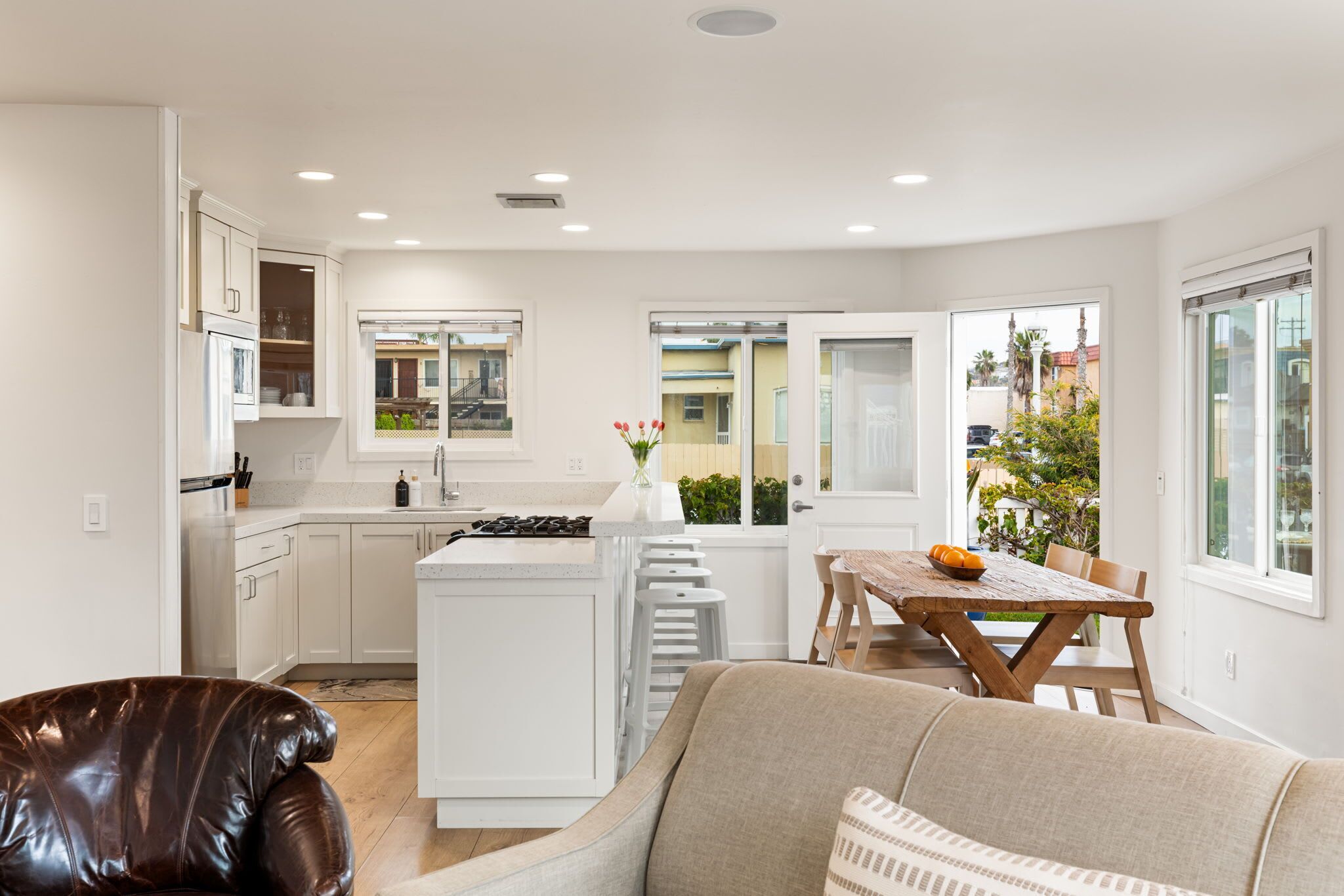 Una cocina moderna con armarios blancos, una isla central y un comedor con mesa y sillas de madera.