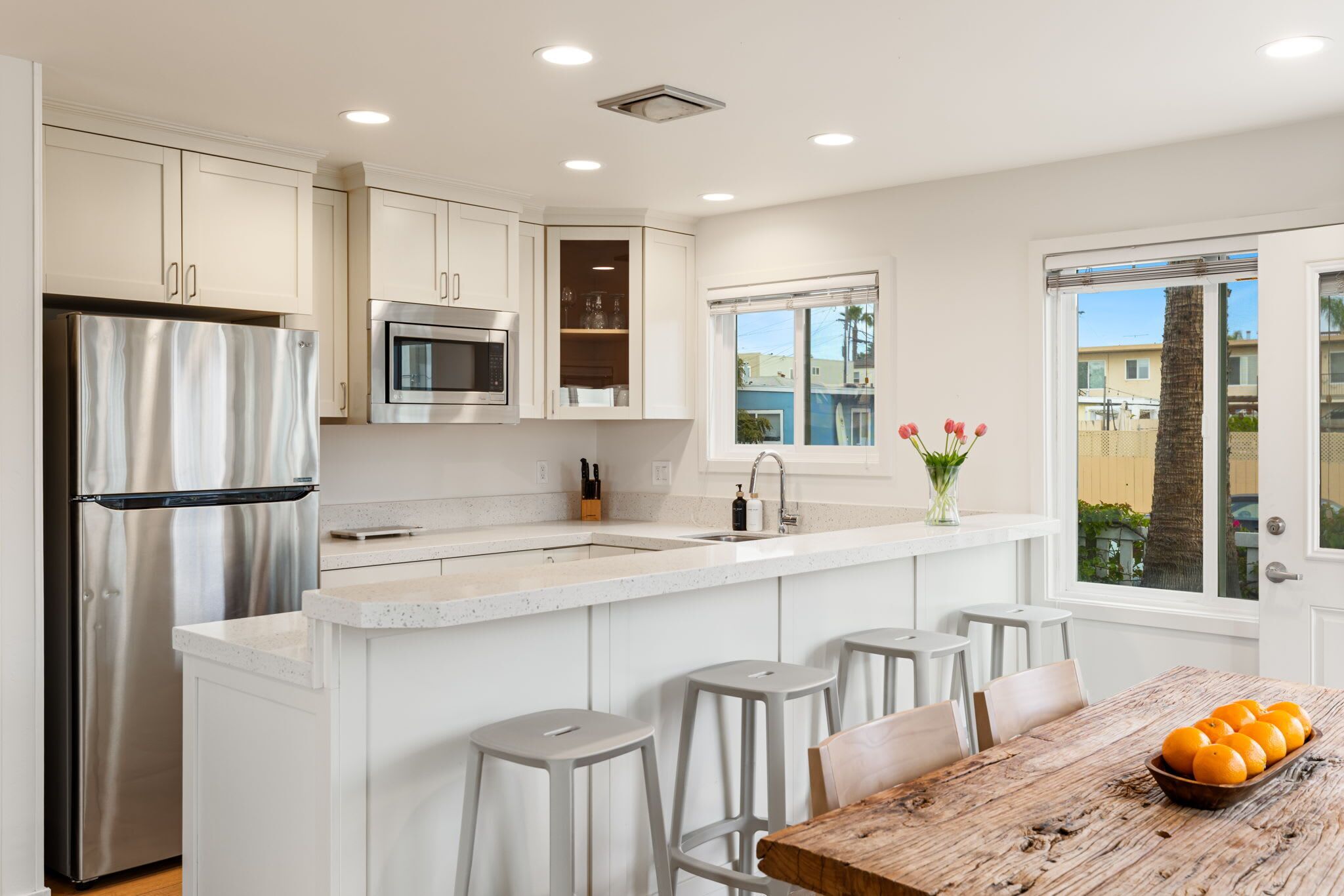 Una cocina moderna con armarios blancos, electrodomésticos de acero inoxidable y una isla central con taburetes de bar.