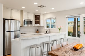 Una cocina moderna con electrodomésticos de acero inoxidable, una isla central con taburetes y vistas a través de un ventanal.