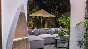 A modern outdoor seating area with a cushioned sofa, a glass table, and a large umbrella. - Villa Rama (by JB Villas) (Bali)