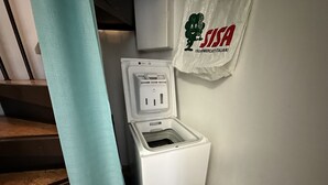 A white portable toilet with a power outlet, a towel hanging on the wall, and a staircase in the background. - Villaggio Tivoli 6-c13 (San Michele al Tagliamento)