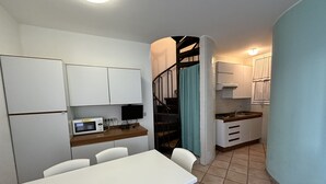 A compact kitchen with white cabinets, a microwave, and a small dining table with chairs. - Villaggio Tivoli 6-c13 (San Michele al Tagliamento)