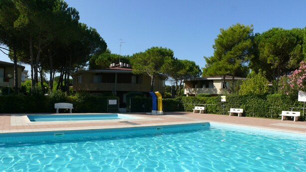 A swimming pool with clear water, surrounded by greenery and buildings. - Villaggio Tivoli 6-c13 (San Michele al Tagliamento)