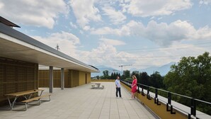 An outdoor terrace with picnic tables, a railing, and a view of mountains. - Ariv Design Apartments (Cham)