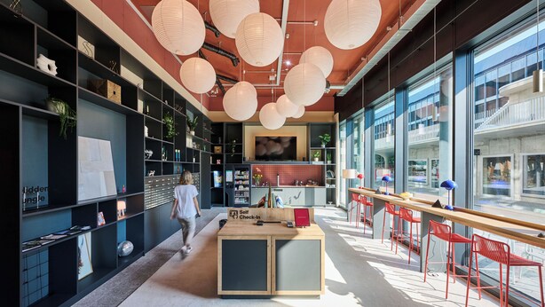 A modern interior with a self-check-in kiosk, red bar stools, and large windows offering views of the city. - Ariv Design Apartments (Cham)