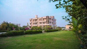 A multi-story residential building with a flat roof, surrounded by a well-maintained lawn and various trees. - The Govindam Resort (Vrindavan)