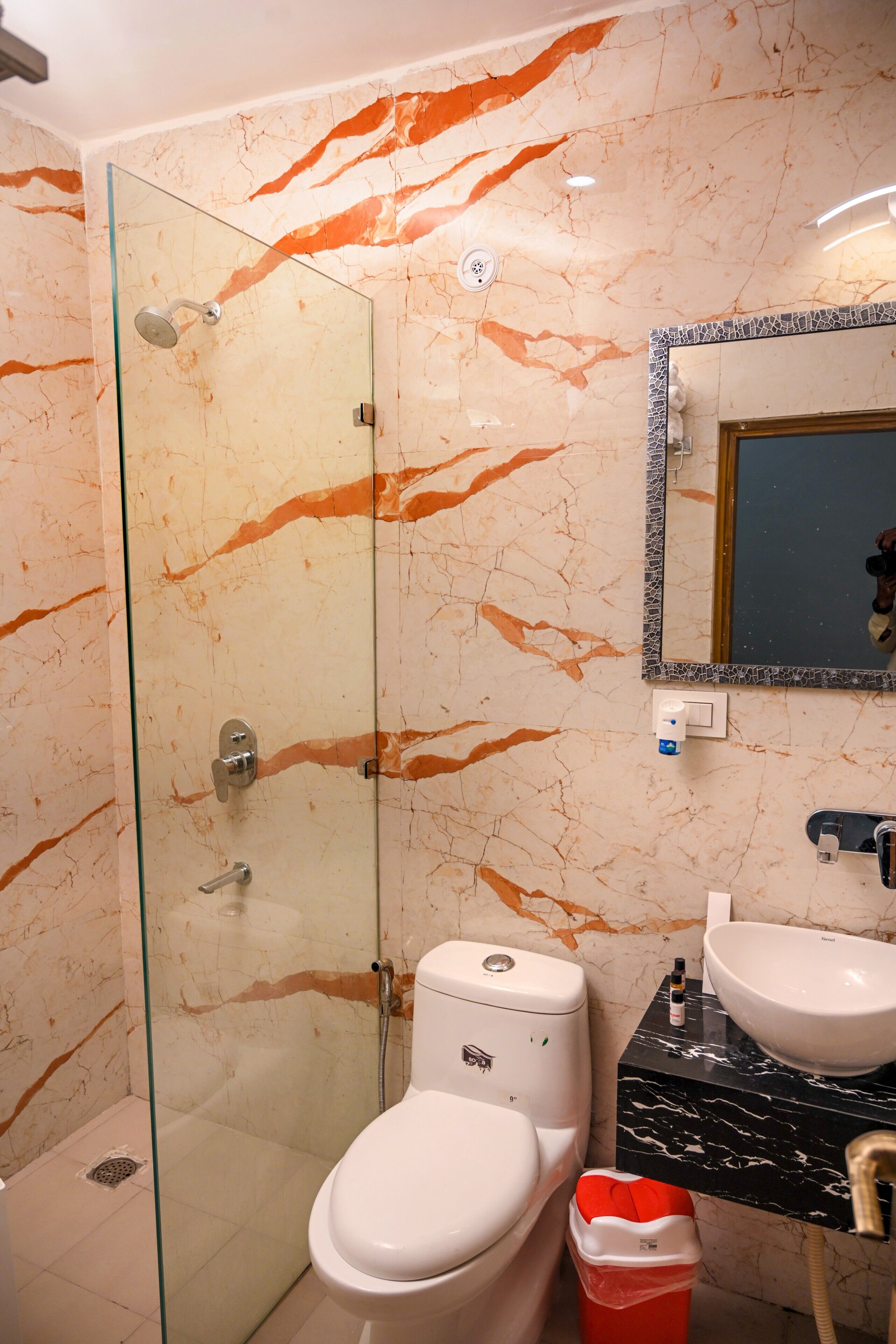 Un baño con ducha envuelta en vidrio, inodoro blanco, lavamanos y un cubo de basura.