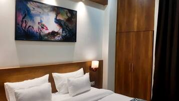 Una habitación de hotel con una cama grande, cabecera de madera, un cuadro colgado en la pared y un armario.