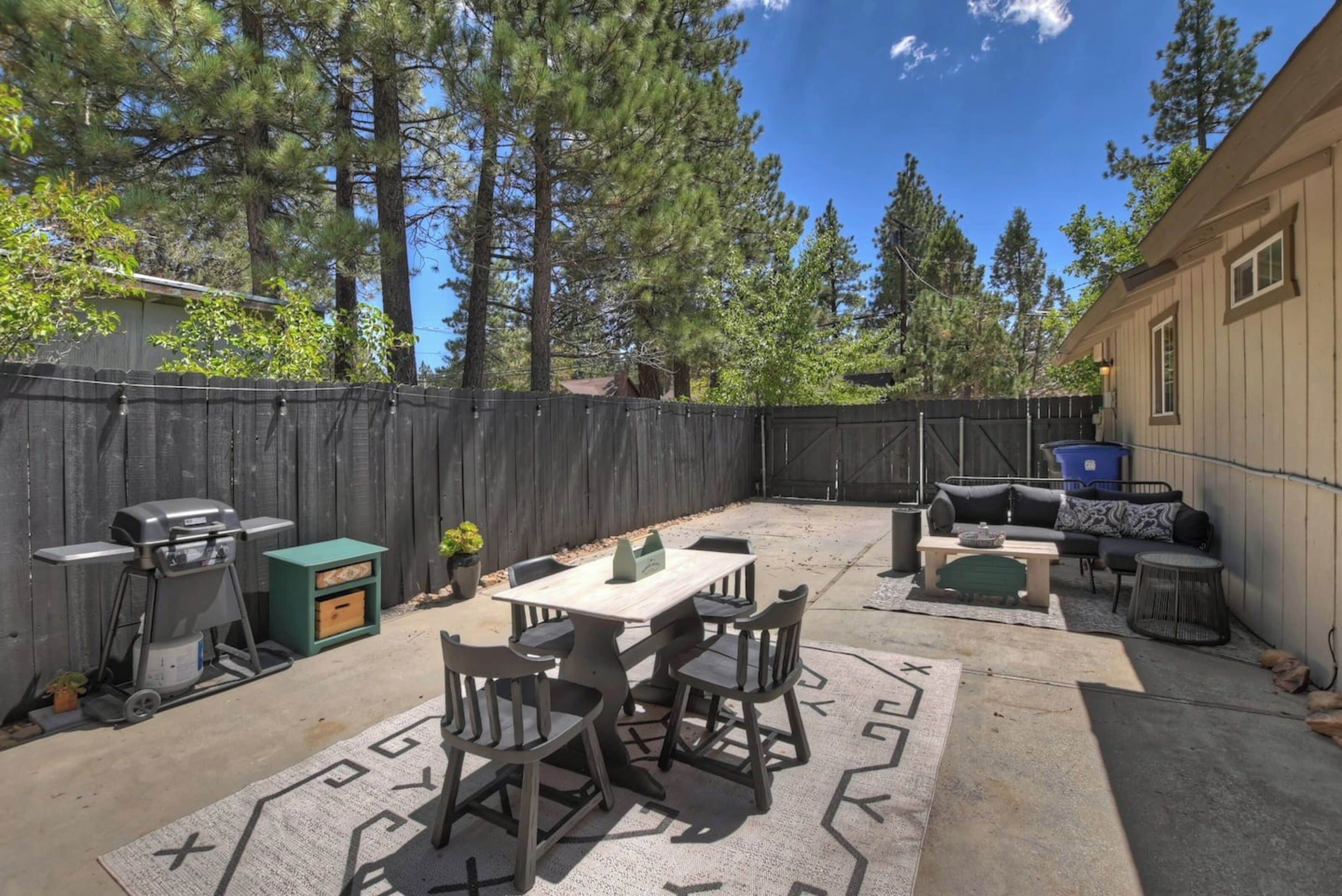 A backyard with a wooden table and chairs, a barbecue grill, and a sofa.