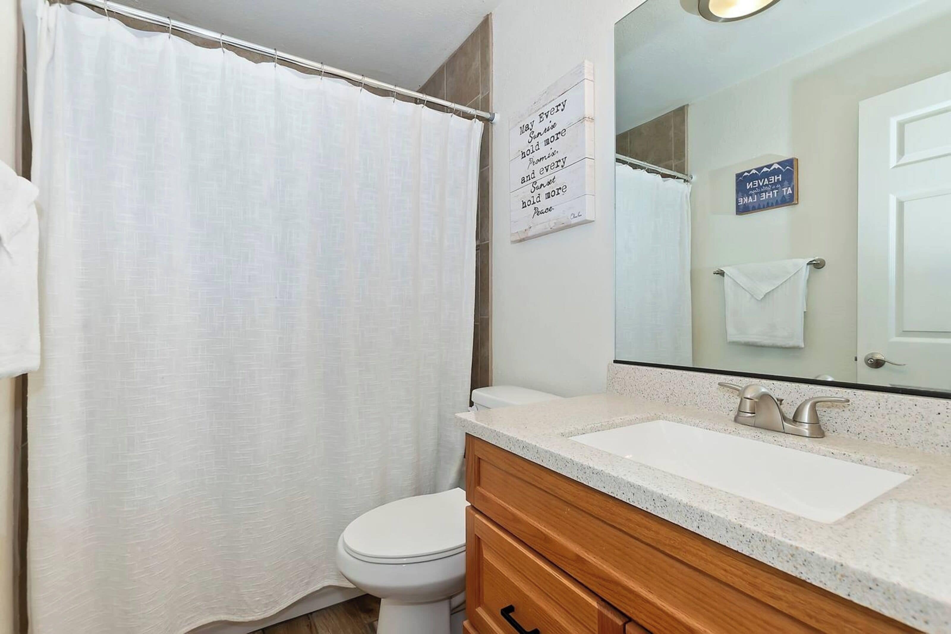 A bathroom with a shower curtain, a toilet, a sink with a mirror, and a towel rack.