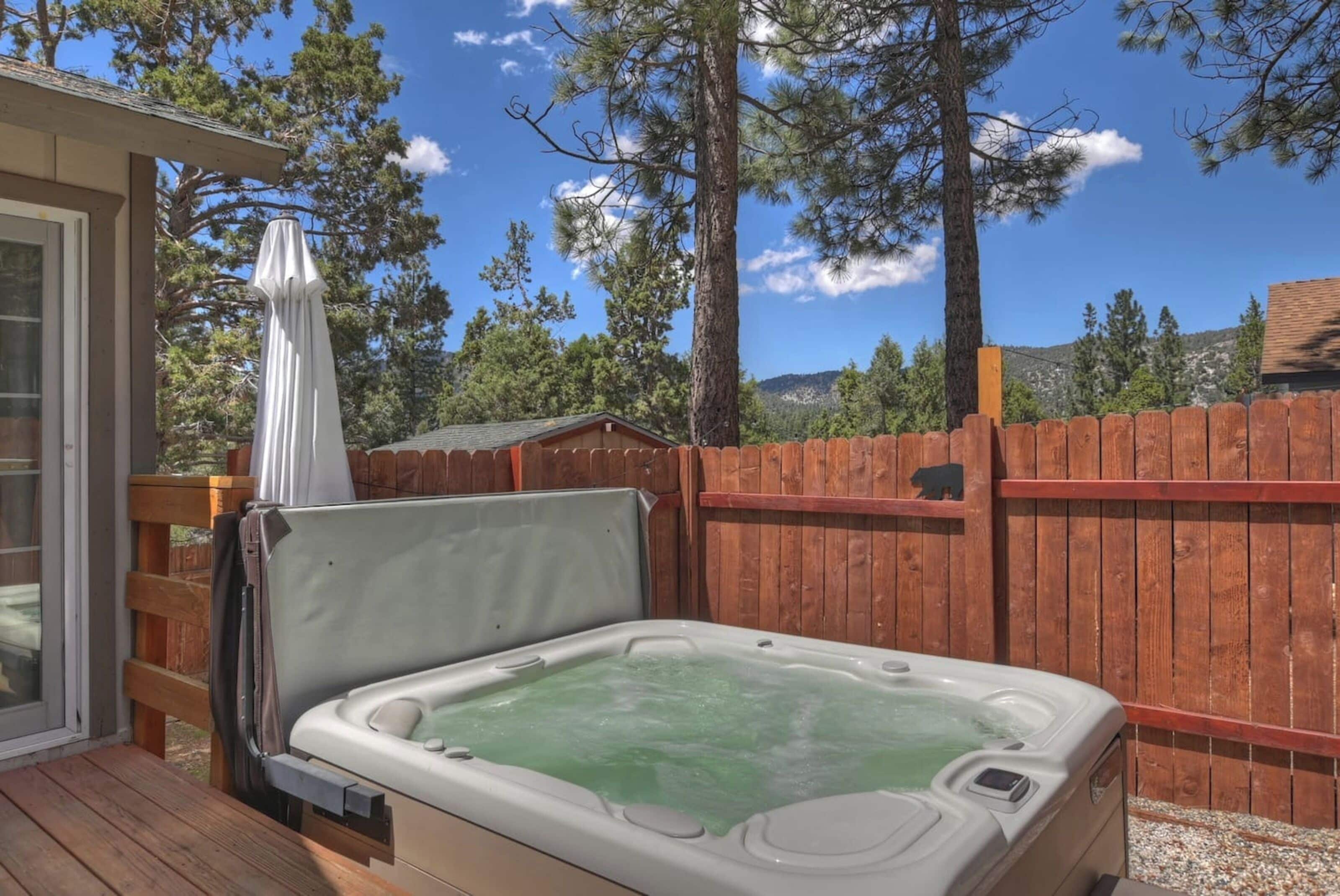 Un jacuzzi en una terraza de madera, con un cerramiento de madera y árboles al fondo.