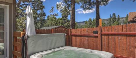 Un jacuzzi en una terraza de madera, con un cerramiento de madera y árboles al fondo.