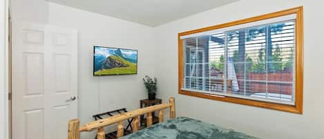 A bedroom with a bed, a window with blinds, a door, and a wall-mounted TV.