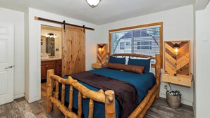 Een slaapkamer met een houten bedframe, een groot raam met jaloezieën, een spiegel en twee wandlampen.