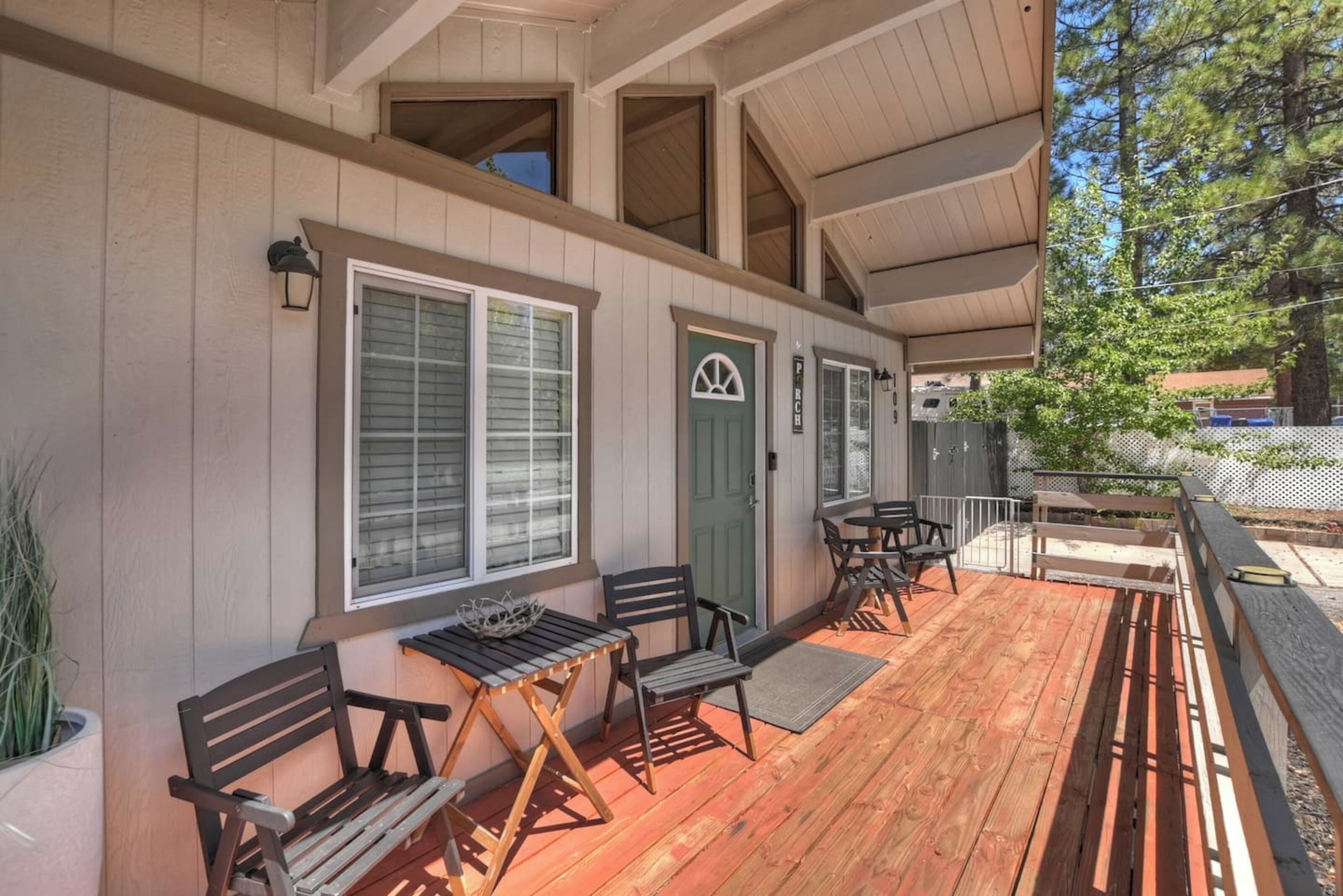A covered outdoor area with wooden benches and tables, a green door, and a window with blinds.
